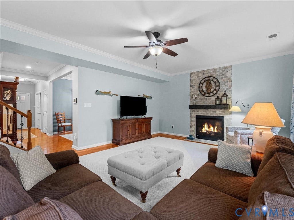 9990 Orchard Meadow Road, Mechanicsville, VA 23116 Built-in fireplace with a stone surround and wood mantel, ceiling fan with integrated lighting, crown molding, and wood-finish flooring