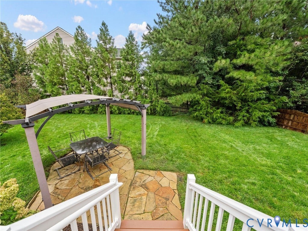 9990 Orchard Meadow Road, Mechanicsville, VA 23116 Expansive backyard featuring a natural flagstone patio, pergola with a fabric canopy, and mature trees providing privacy
