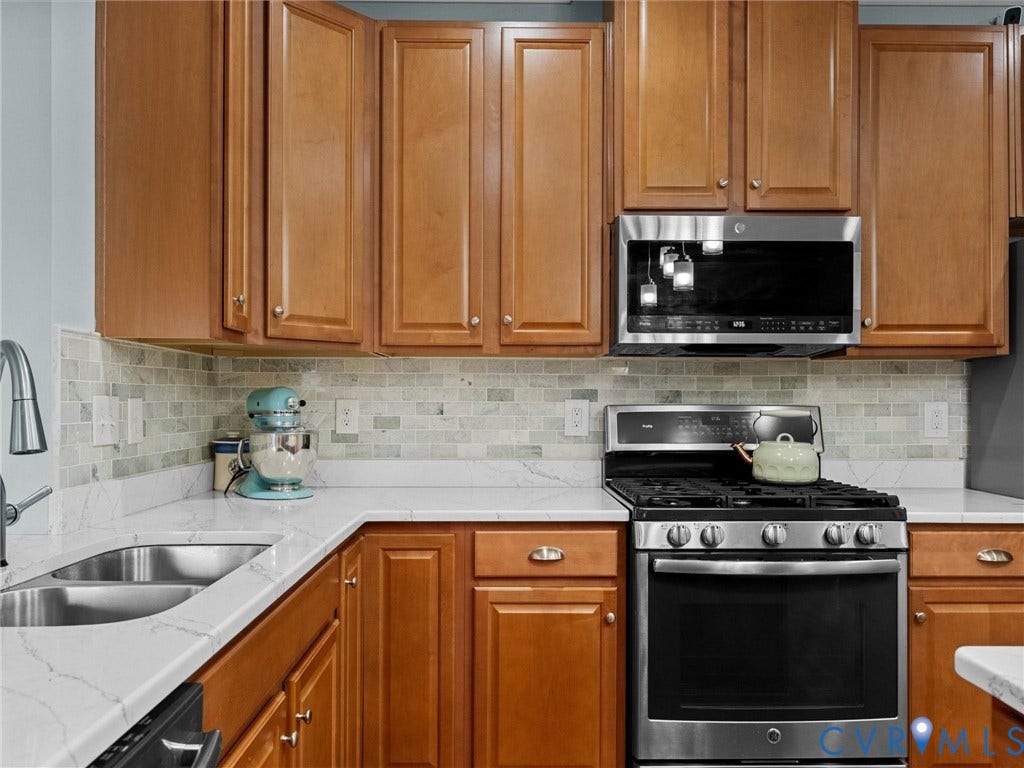 9990 Orchard Meadow Road, Mechanicsville, VA 23116 Wood-finish cabinetry, stainless steel appliances, white countertop, and tiled backsplash