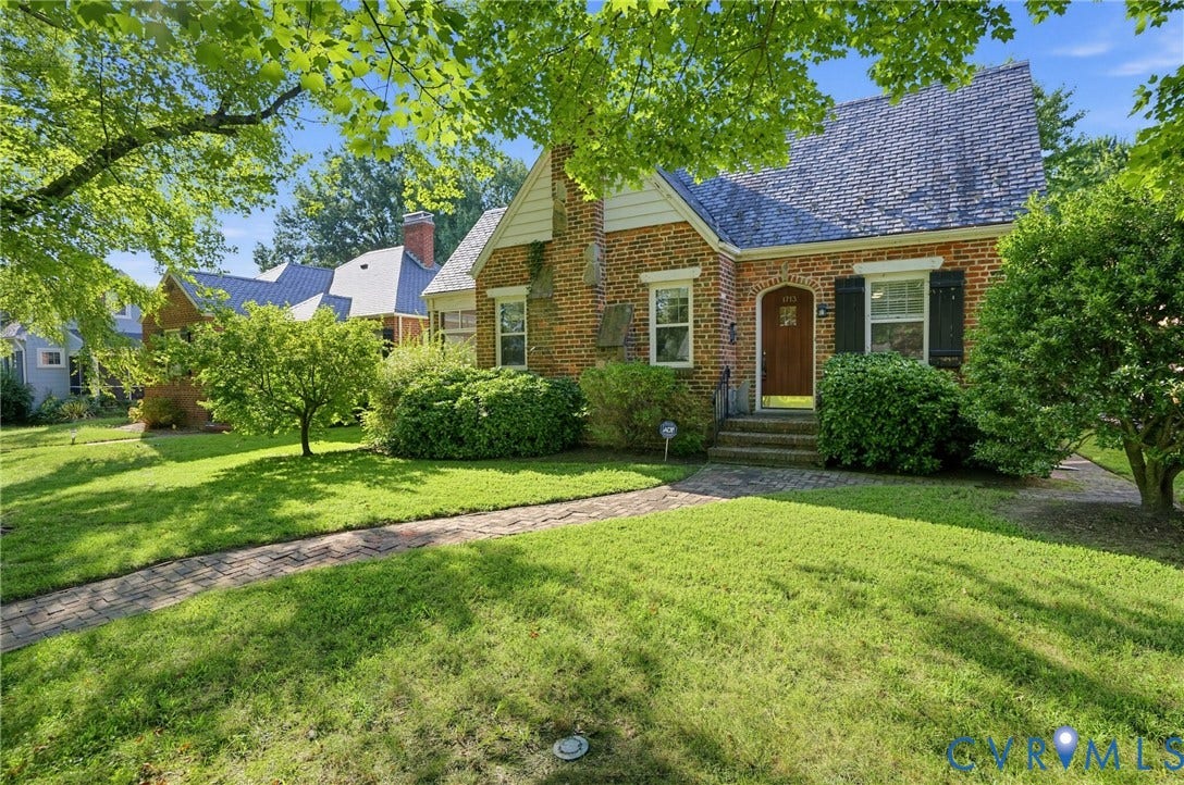 1713 Wilmington Avenue, Richmond, VA 23227 Brick facade featuring a steep-pitched roof, arched wooden entry door, and dark shutters