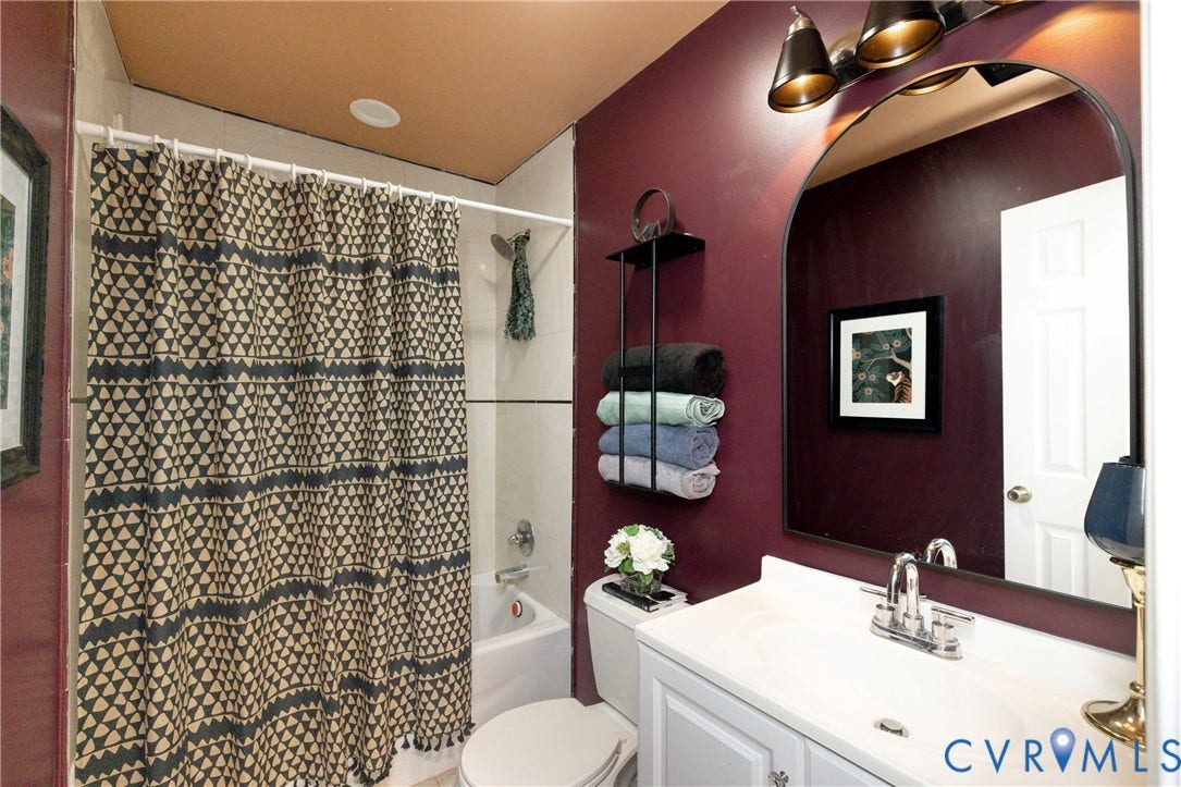 2127 Wright Avenue, Bellemeade, Richmond, VA 23224 Spa-inspired bathroom featuring deep burgundy accent walls, a white vanity with integrated sink and chrome faucet, large framed mirror with integrated lighting, and a walk-in shower with geometric tile surround and dual showerheads