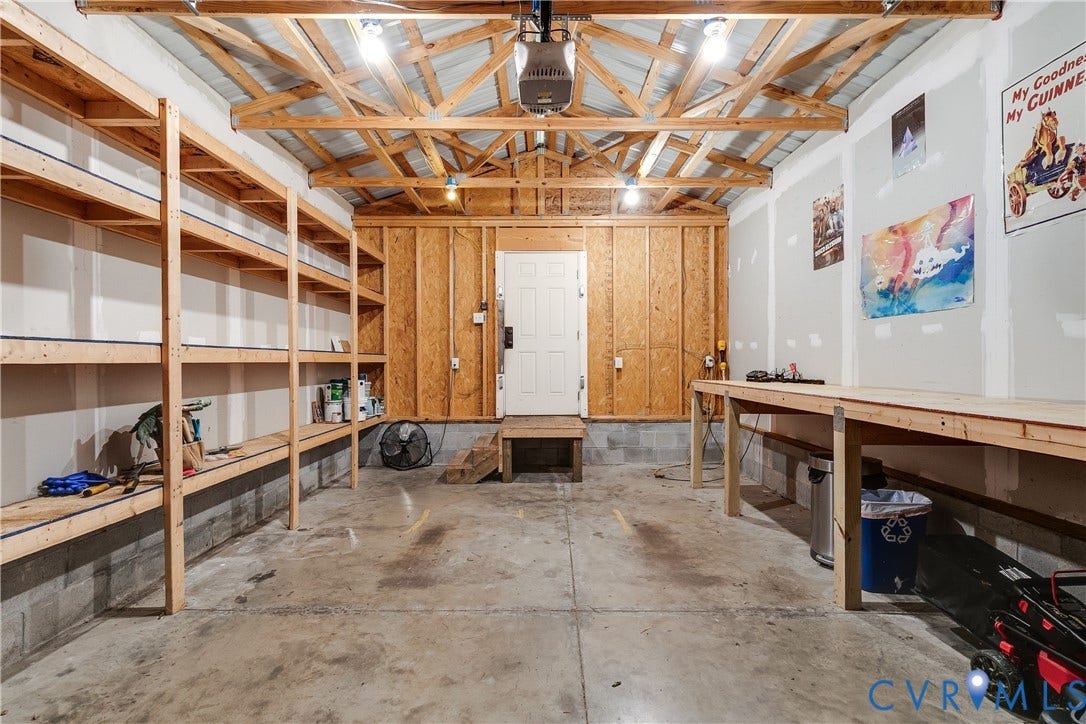 1311 N 33rd Street, Oakwood, Richmond, VA 23223 Garage featuring exposed wood beam ceiling, concrete floor, overhead lighting, extensive built-in shelving, and a built-in workbench