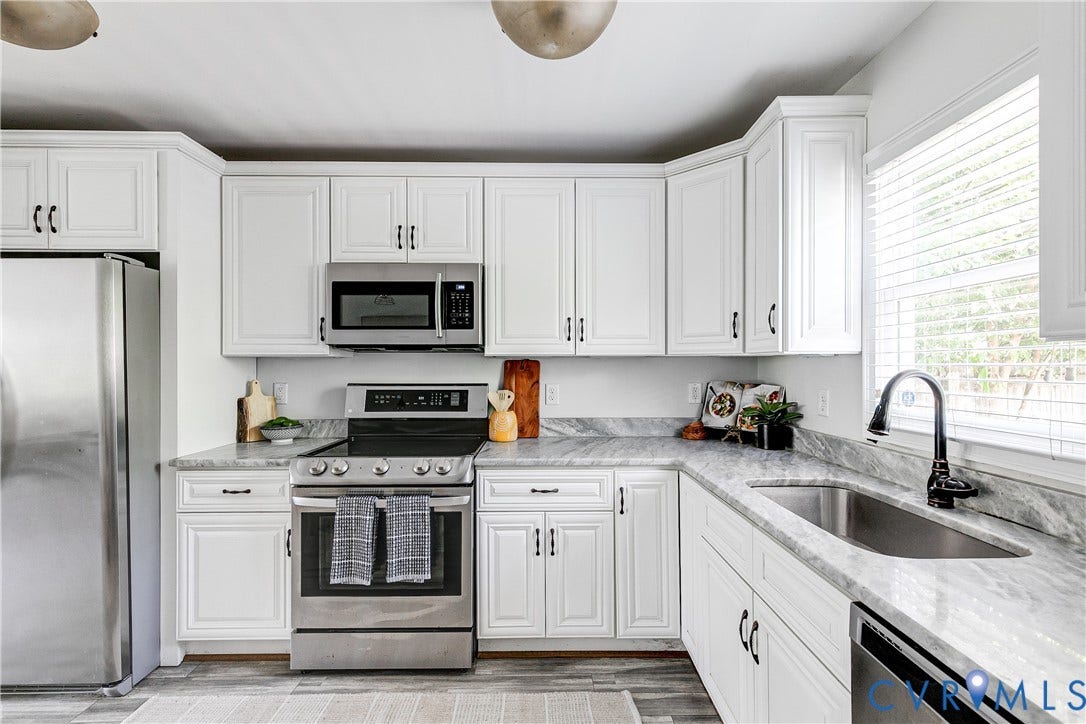 1311 N 33rd Street, Oakwood, Richmond, VA 23223 White cabinetry with dark hardware, stainless steel appliances, undermount sink with gooseneck faucet, light-toned countertops, and wood-finish flooring