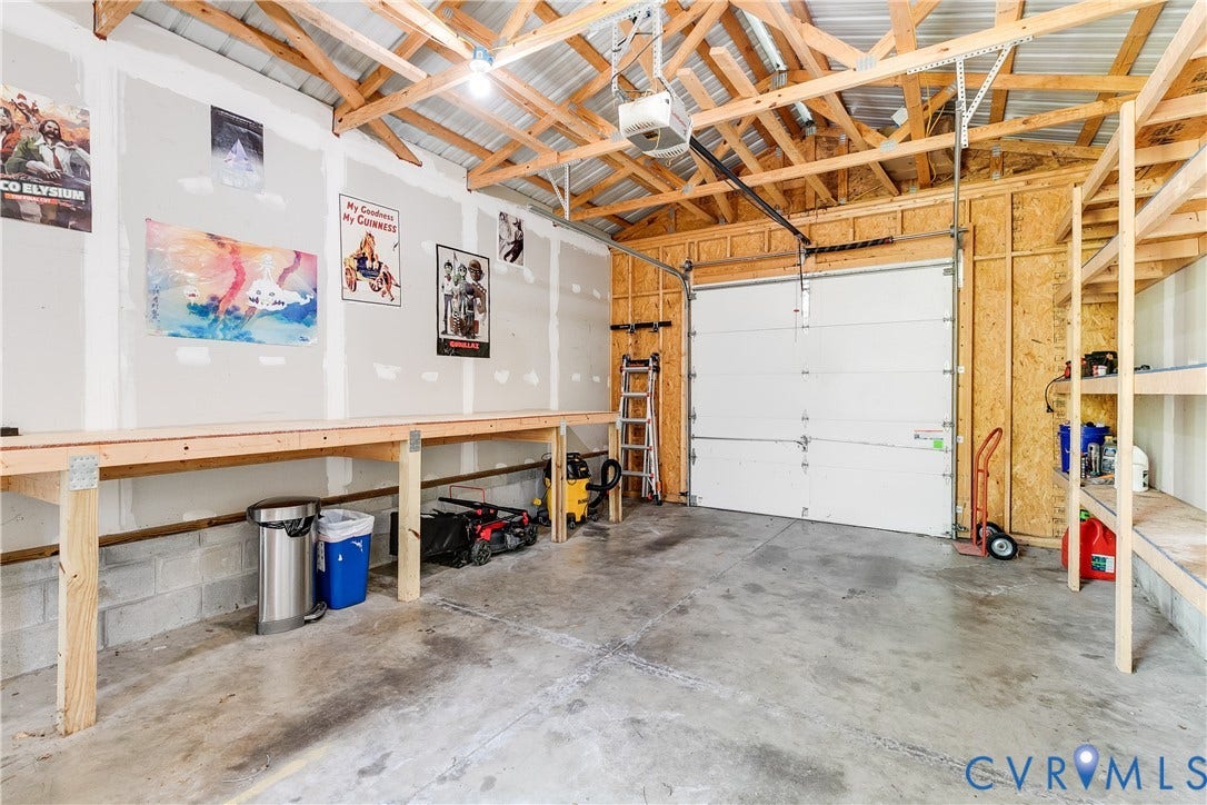 1311 N 33rd Street, Oakwood, Richmond, VA 23223 Garage space featuring exposed wood rafter ceiling, concrete flooring, built-in wooden shelving, a built-in wooden workbench, and an overhead garage door with an automatic opener