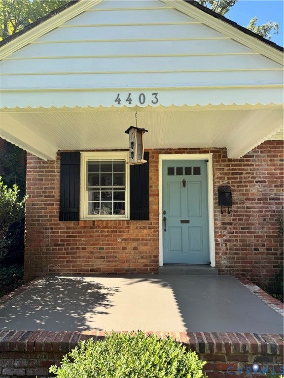 4403 Park Avenue, Richmond, VA 23221 Brick exterior with a light blue entry door, featuring a covered porch, white scalloped trim, and a window with dark shutters