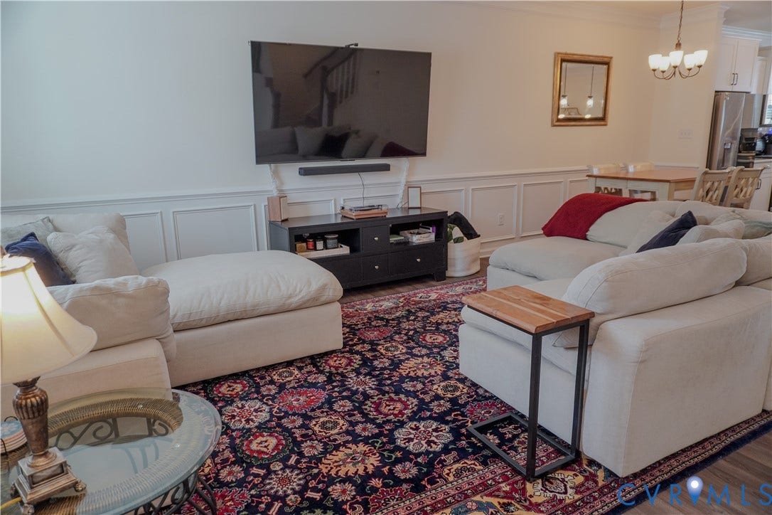 Wainscoting wall treatment, wood-finish flooring, built-in media console, and an attached chandelier