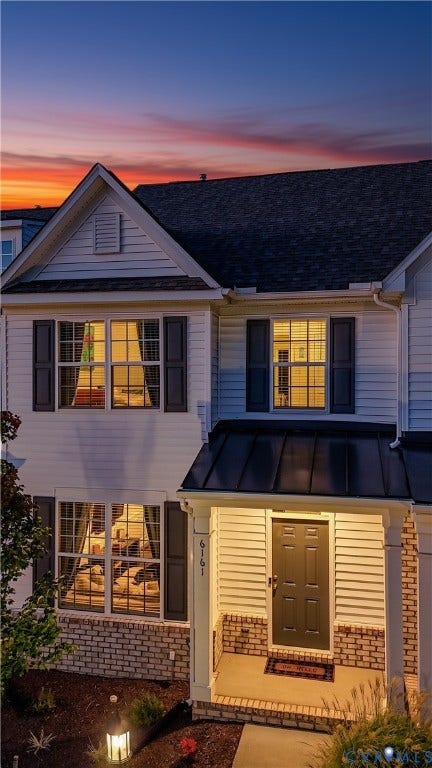 White siding exterior with dark shutters, covered entry with a dark door, and brick detailing