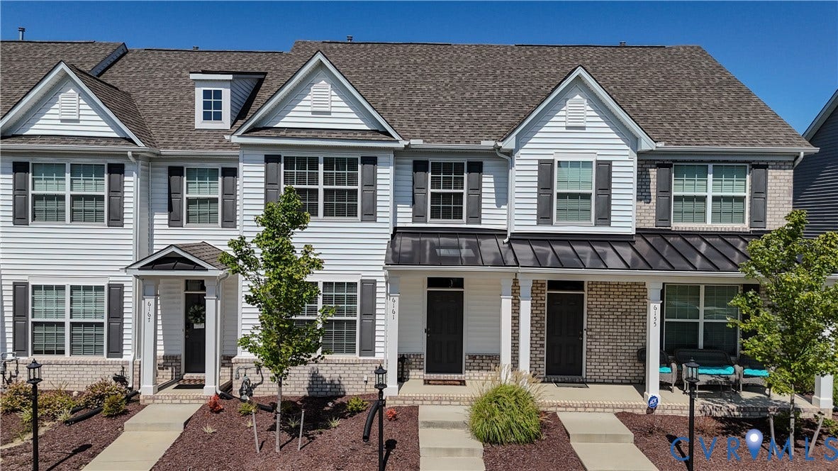 White siding exterior with a shingle roof, dark shutters, and brick accents