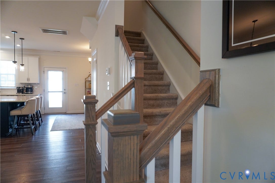Wood-finish flooring leading to a kitchen with white cabinetry and dark base cabinets