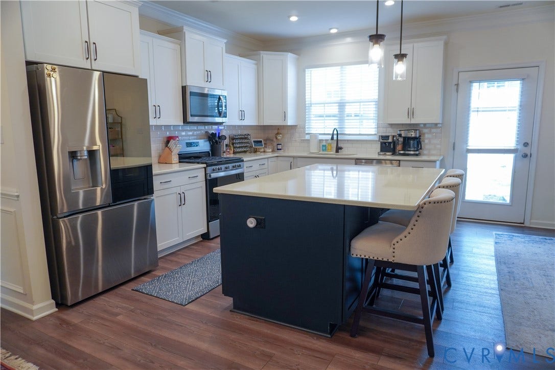 White cabinetry with dark hardware, stainless steel appliances, light-toned countertops, and wood-finish flooring