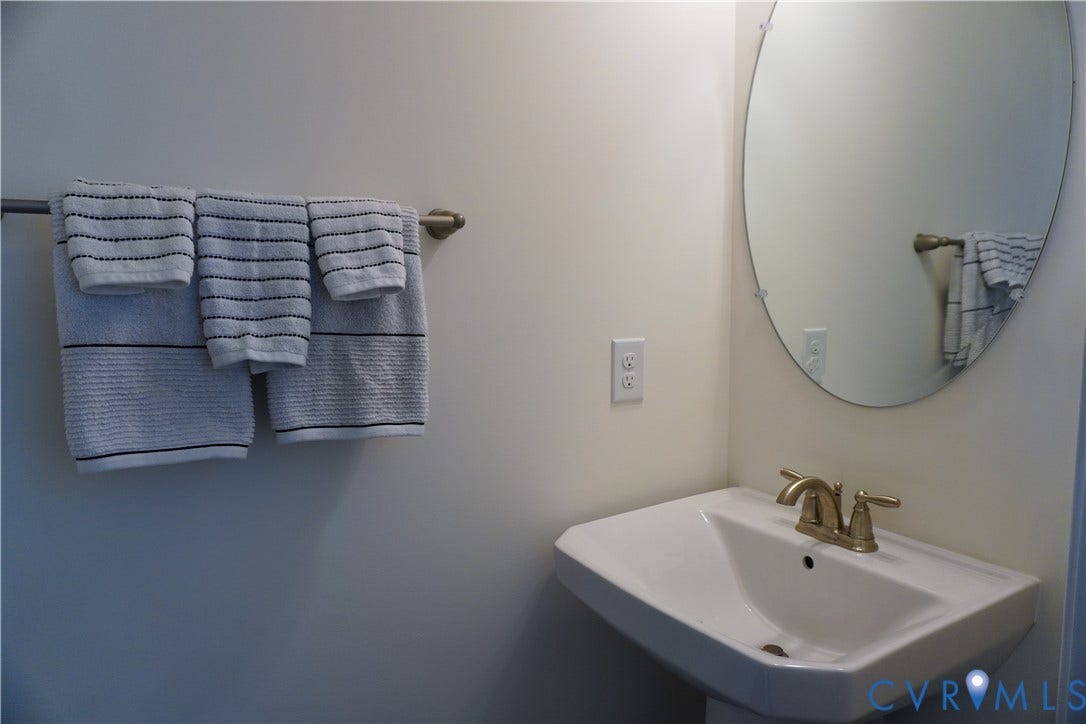 Pedestal sink with a dual-handle faucet, oval wall mirror, and wall-mounted towel bar
