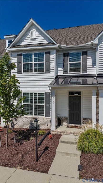 White vinyl siding exterior with dark shutters, a dark entry door, and a metal awning