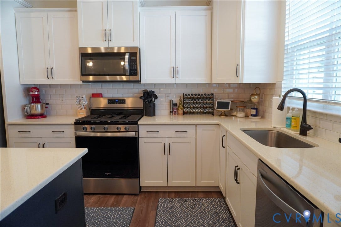 White cabinetry, stainless steel appliances, solid surface countertops, subway tile backsplash, and wood-finish flooring