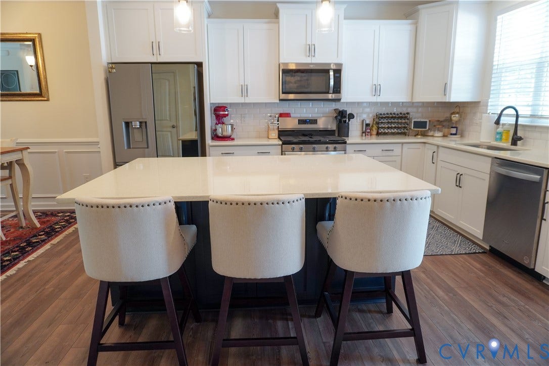 Kitchen featuring wood-finish flooring, white cabinetry, a central island with a light-colored countertop, and stainless steel appliances