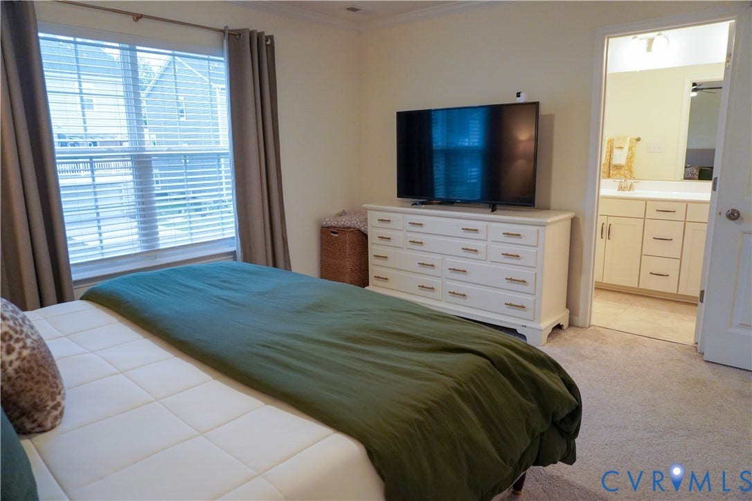 Spacious room featuring carpeting, a large window with blinds, and direct access to a bathroom with a vanity and mirror