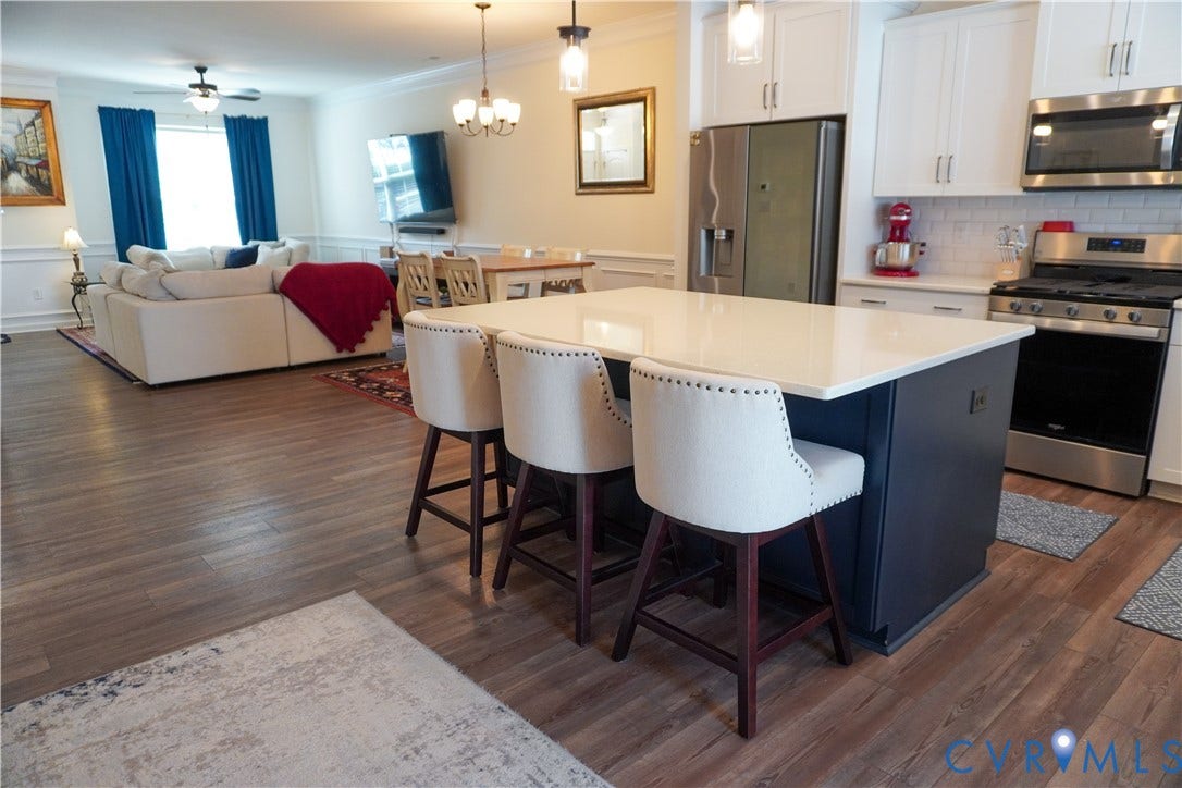 Kitchen island with a white countertop and dark base, stainless steel appliances, white upper cabinetry, and wood-finish flooring