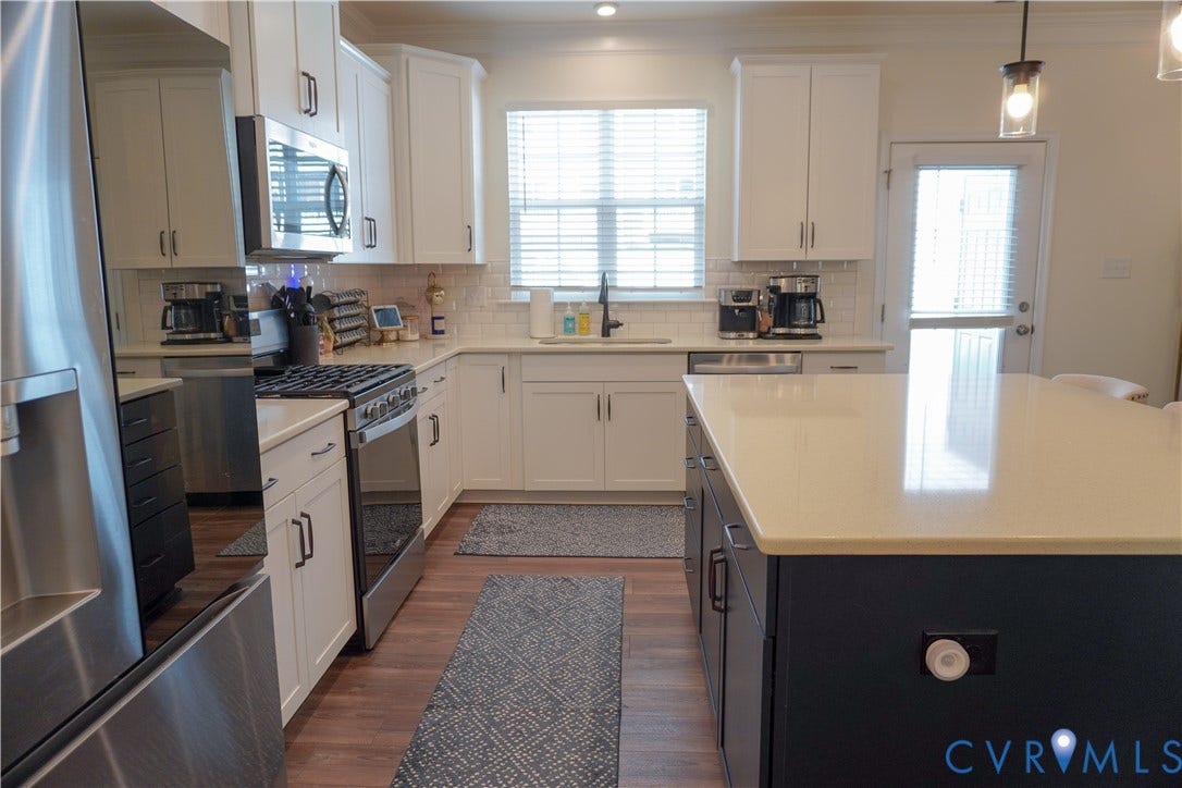 Kitchen featuring white cabinetry, stainless steel appliances, an island with countertop, subway tile backsplash, and wood-finish flooring