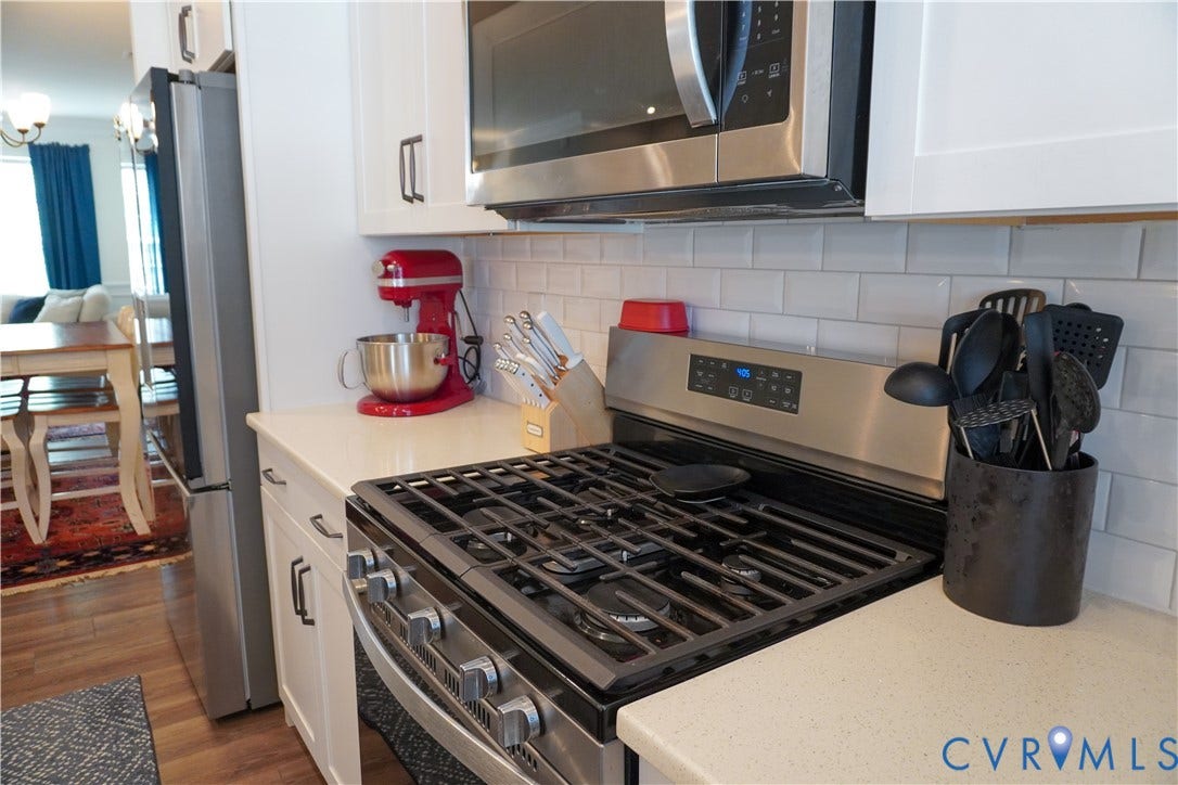 Stainless steel gas range, microwave, and refrigerator with white shaker cabinetry, light-toned countertops, and subway tile backsplash