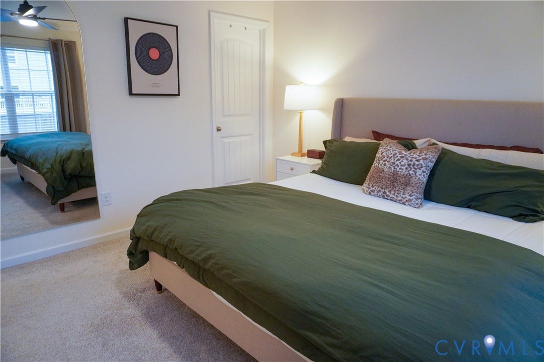 Plush carpeting, paneled interior door, large window with blinds, and ceiling fan