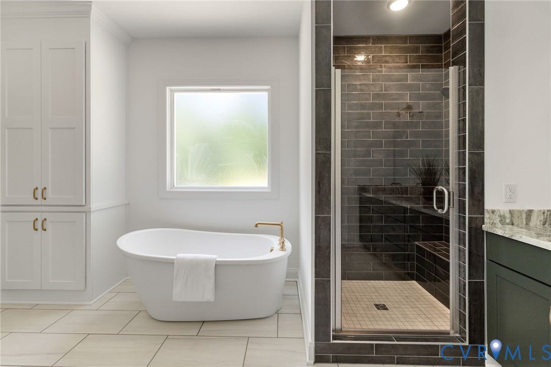 12506 Ashton Dell Road, Chester, VA 23831 Freestanding soaking tub with gold-finish fixtures, a walk-in shower with dark subway tile, glass enclosure, and built-in bench, along with white built-in cabinetry, and tile flooring