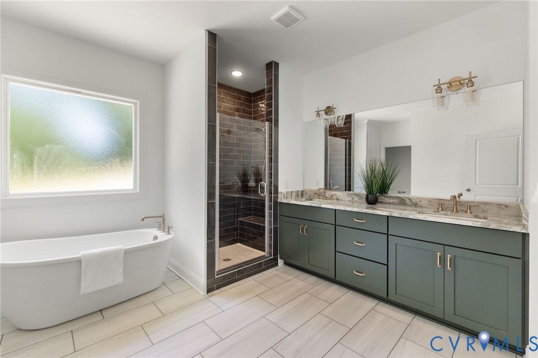 12506 Ashton Dell Road, Chester, VA 23831 Freestanding soaking tub, walk-in shower with dark tile surround, dual vanity with green cabinetry, large integrated mirror, and light tile flooring