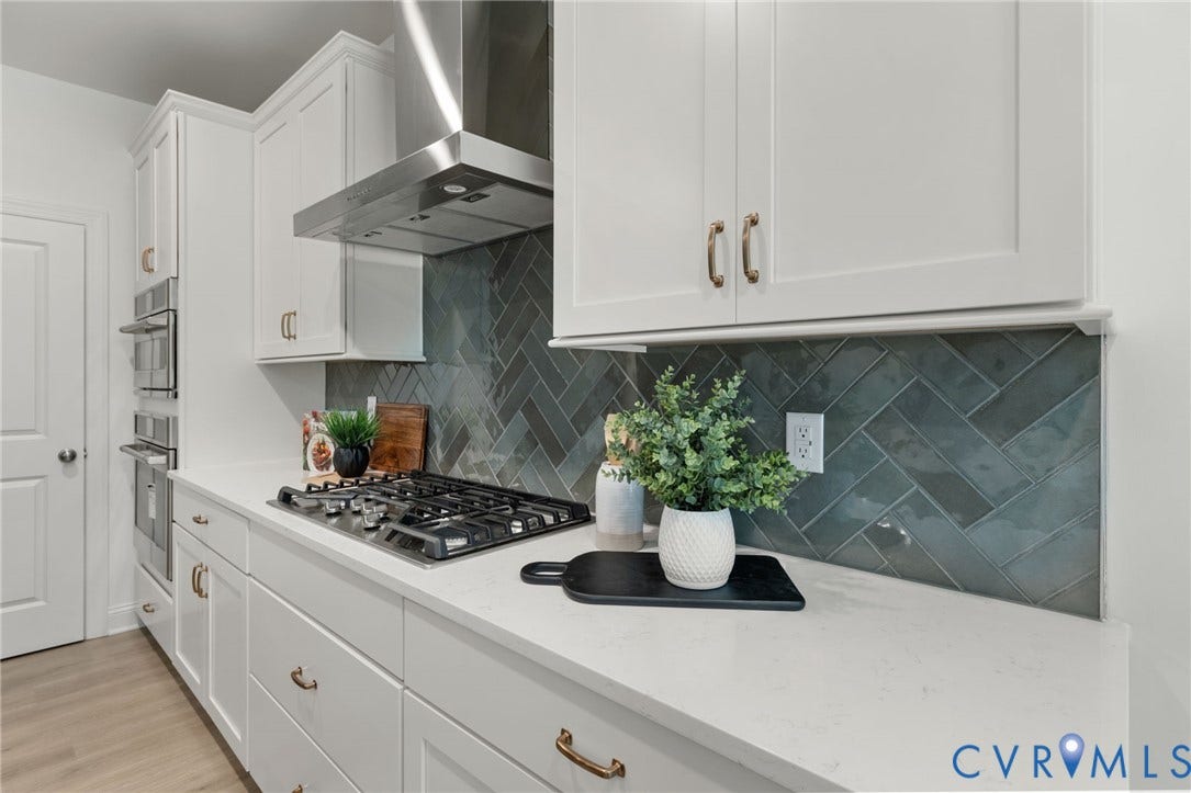 12506 Ashton Dell Road, Chester, VA 23831 White cabinetry with brass-finish hardware, stainless steel range hood, herringbone pattern tile backsplash, gas cooktop, and built-in double ovens