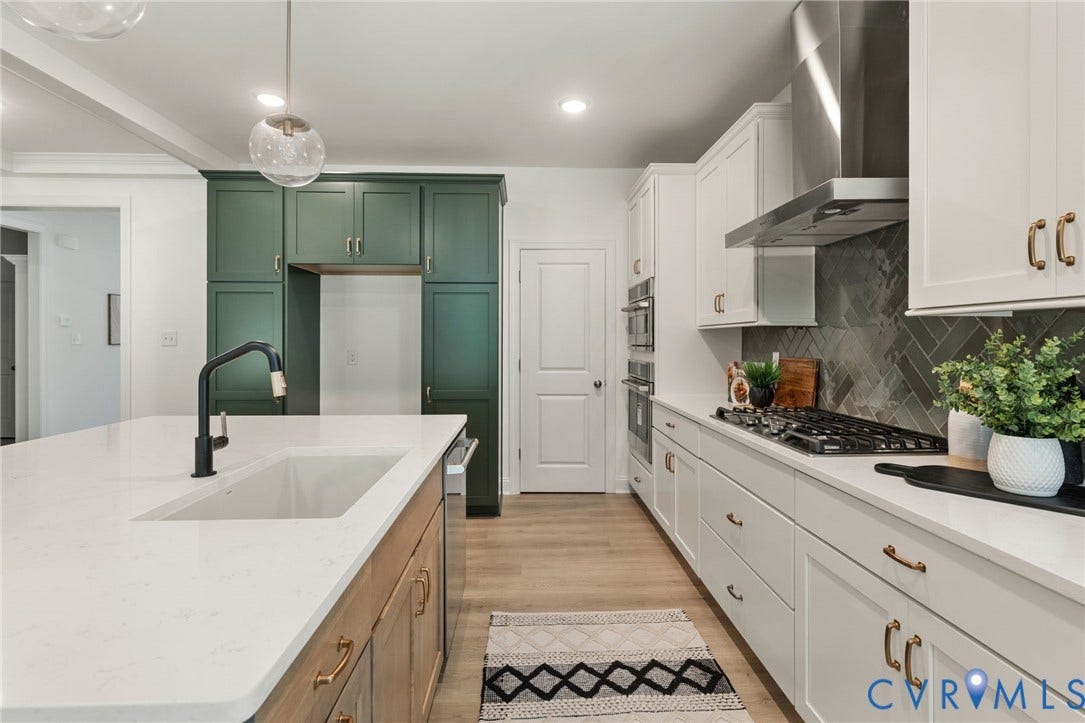 12506 Ashton Dell Road, Chester, VA 23831 Gourmet kitchen featuring white shaker cabinetry, an expansive center island with an undermount sink, quartz countertops, a herringbone tile backsplash, and stainless steel appliances
