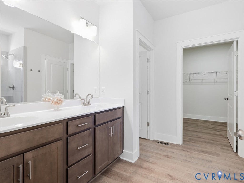 3102 Kensington Lane, Goochland, VA 23063 Dual sink vanity with dark wood-finish cabinetry, a single expansive mirror, and light wood-finish flooring