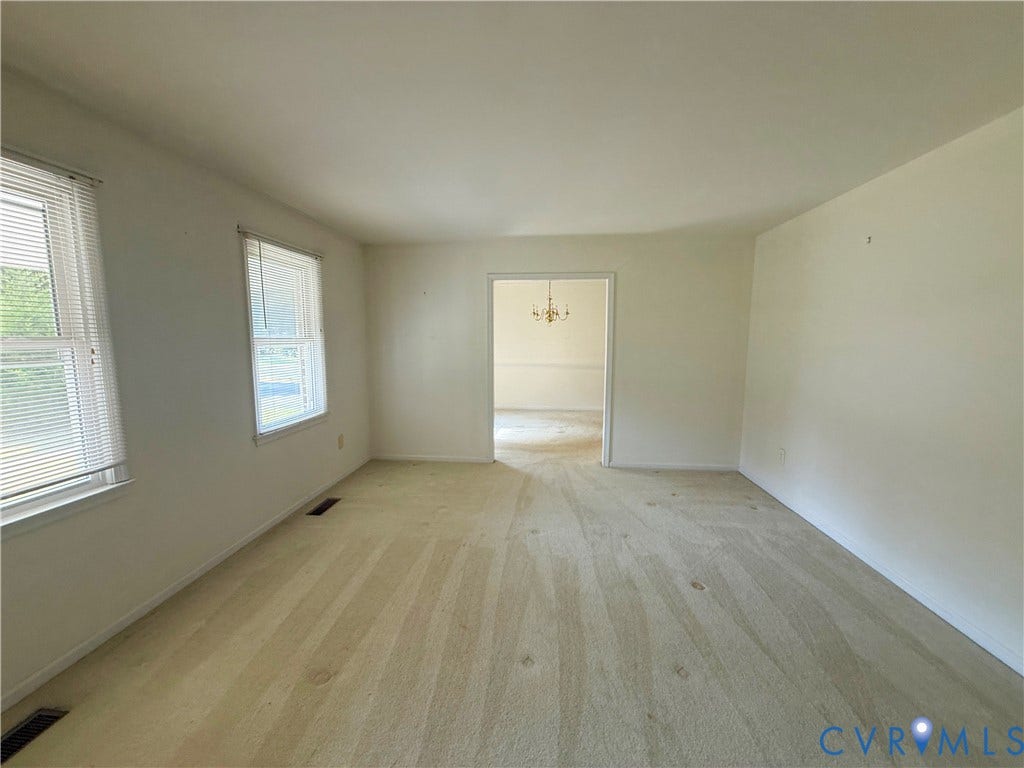 4512 Greenbriar Drive, Chester, VA 23831 Bright interior space with two windows, light-toned carpeting, and a doorway leading to an additional area featuring a chandelier