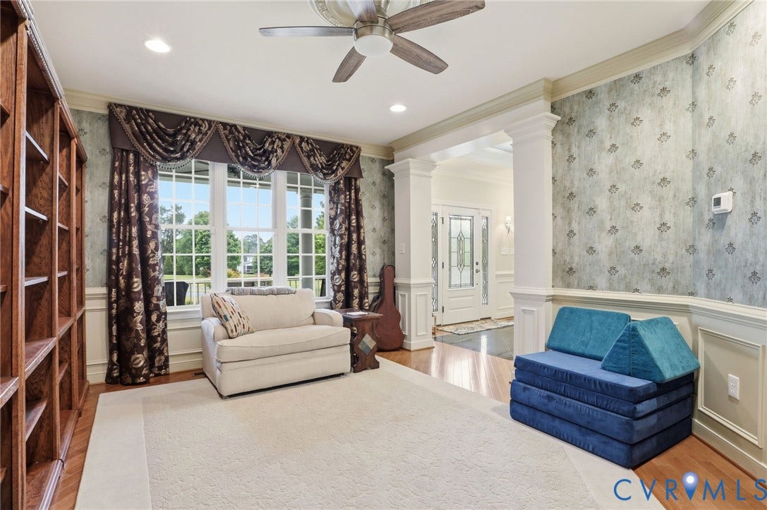 Hardwood flooring, crown molding, built-in shelving, decorative wallpaper, and ceiling fan with integrated lighting