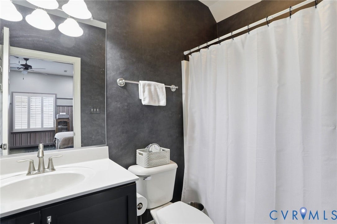Bathroom featuring a vanity with a white countertop, wall-mounted mirror, and a shower with a white curtain
