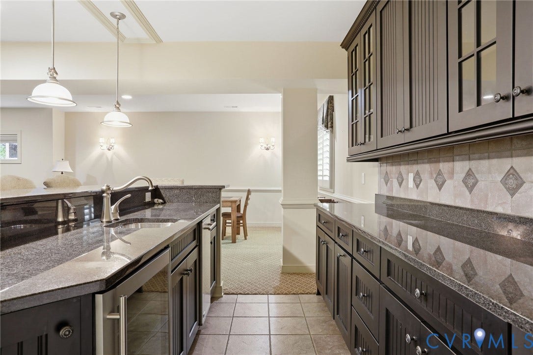 Wet bar featuring dark cabinetry, stone countertops, a tile backsplash, and a stainless steel sink with a gooseneck faucet