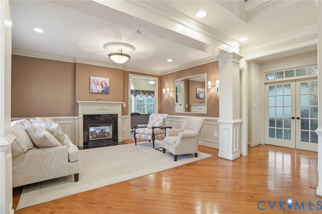 Hardwood flooring, decorative columns, wall paneling, a fireplace with a stone surround, and French doors with frosted glass panels
