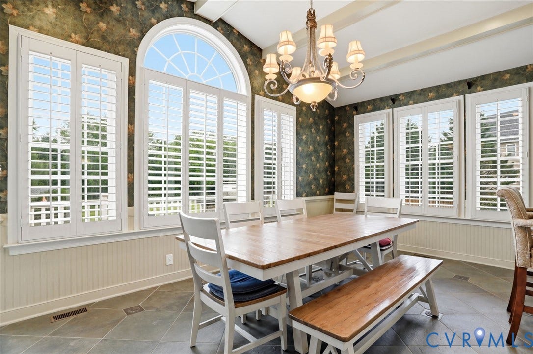 Arched window with plantation shutters, tile flooring, beadboard wainscoting, and a decorative chandelier