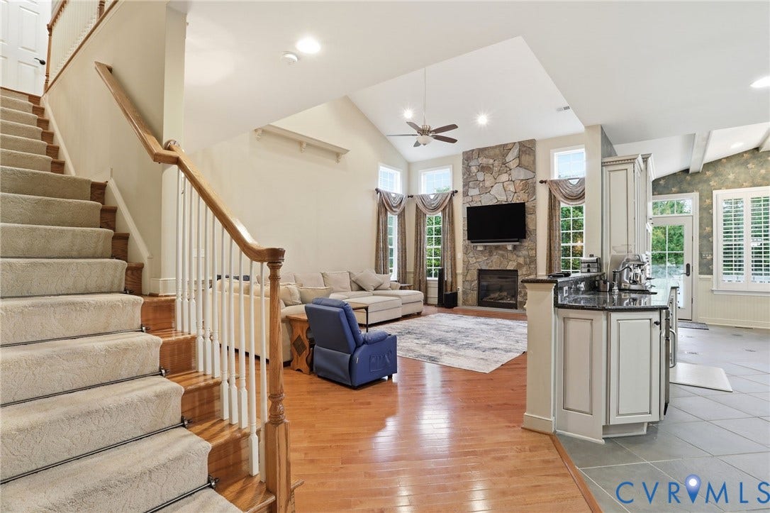 Hardwood flooring, stone fireplace, vaulted ceiling, built-in cabinetry, and a carpeted staircase with a wood banister