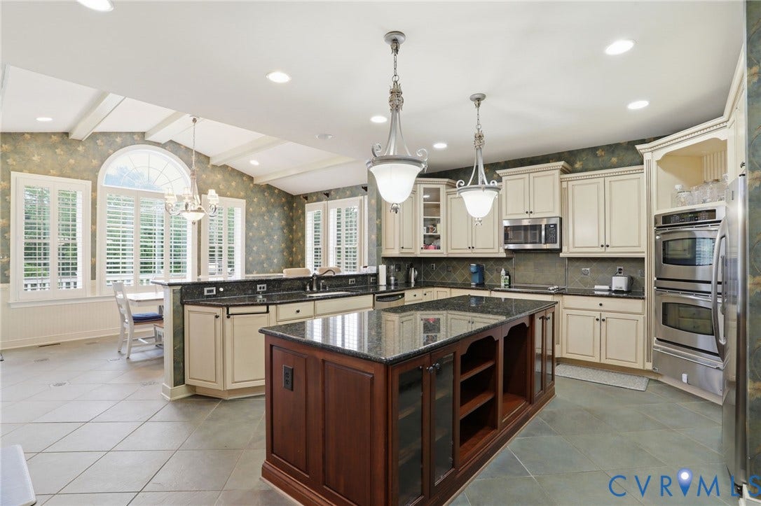 Kitchen featuring a central island with built-in storage, granite countertops, cream-painted cabinetry, and a suite of stainless steel appliances including double wall ovens