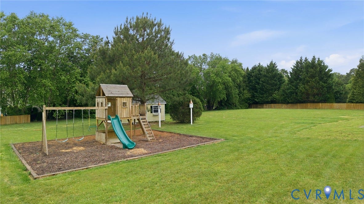 Expansive lawn area featuring a wooden playset with a slide and swings, a small shed structure, and a perimeter fence