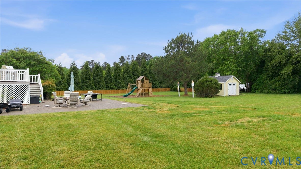 Expansive green lawn with a gravel patio, raised deck with white railings, and a detached shed