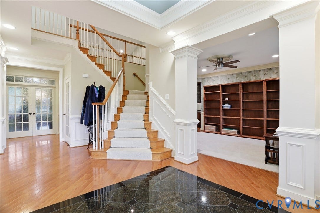 Hardwood flooring with a black tile inlay, carpeted staircase with wood banister, built-in bookshelves, and recessed lighting