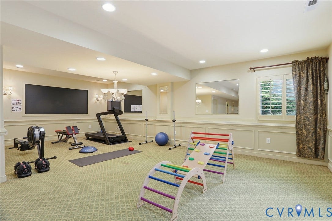 Recessed lighting, wall sconces, window with plantation shutters, decorative wall paneling, and a patterned carpeted floor