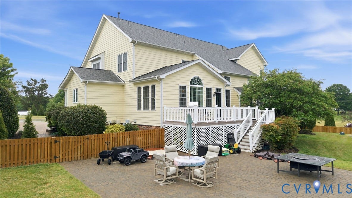 Expansive paver patio with a wood privacy fence, leading to a multi-level deck with white railings and lattice skirting
