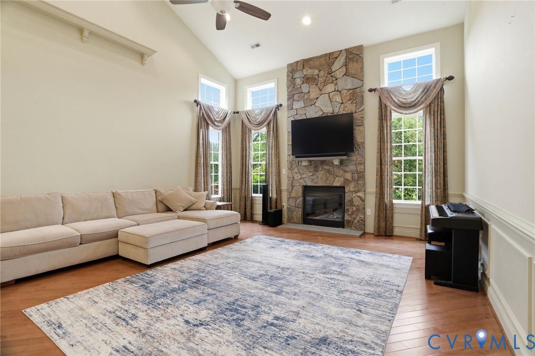 Vaulted ceiling with a ceiling fan, stone-clad fireplace, wood-finish flooring, and multiple large windows