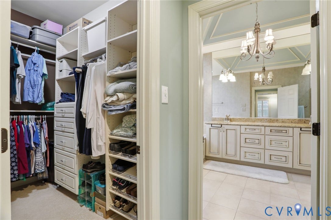 Custom closet organization system and an adjacent bathroom featuring a double vanity with stone countertops, tile flooring, and a coffered ceiling