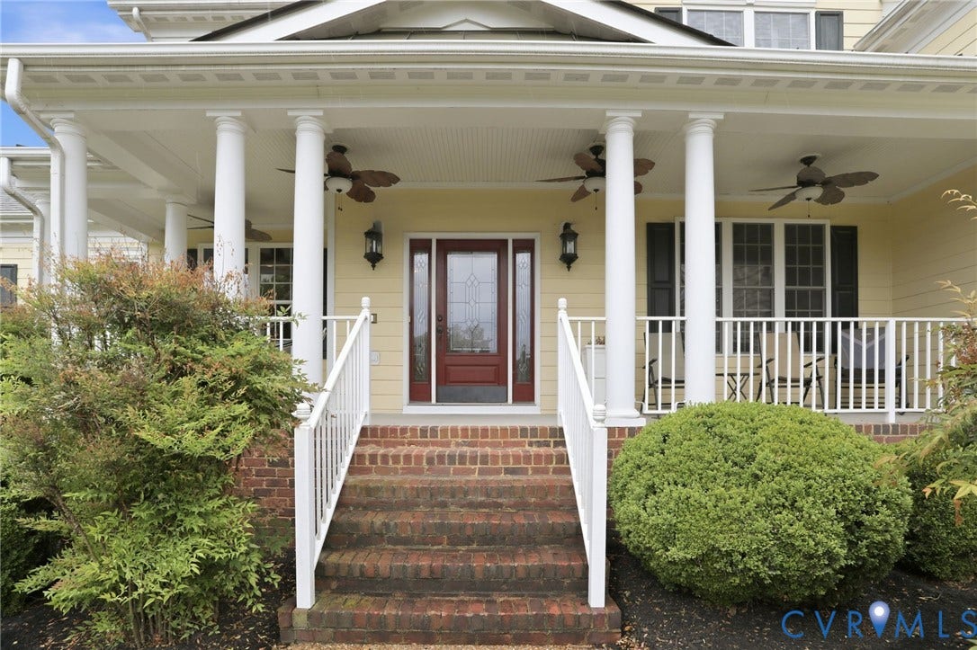 Inviting front porch featuring a brick staircase, white railings, stately columns, and ceiling fans