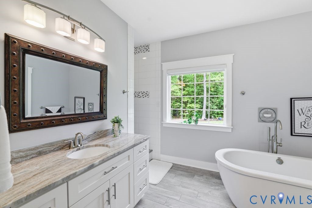 13114 Spring Road, Barr Brook Farms, Rockville, VA 23146 Freestanding bathtub, wood-finish flooring, white vanity with stone countertop, large mirror, and a window with grid panes