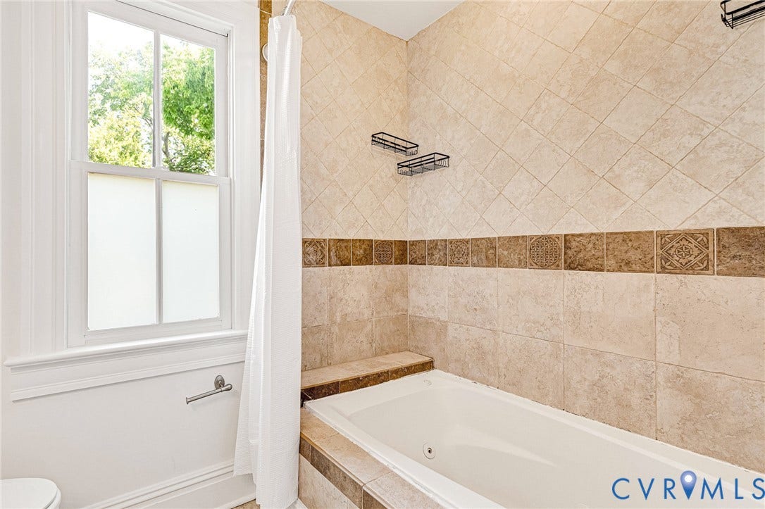 615 N 23rd Street, Church Hill Central, Richmond, VA 23223 Built-in soaking tub with tiled surround, full-height tiled shower walls with decorative accent band, and a double-hung window