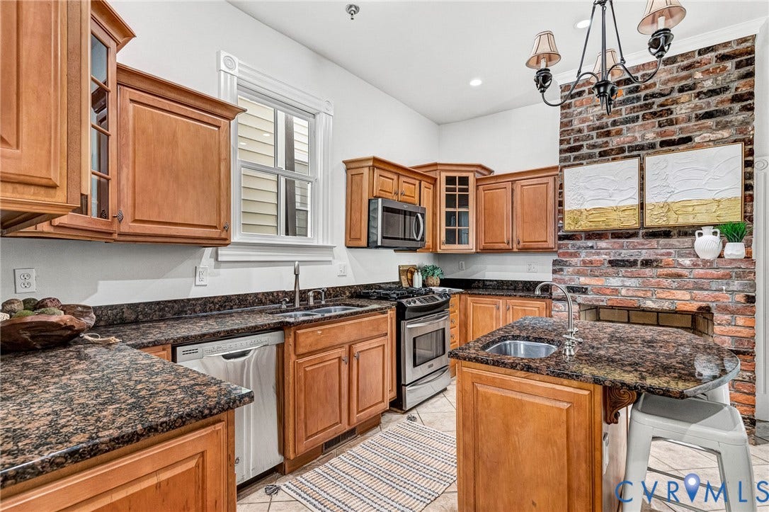 615 N 23rd Street, Church Hill Central, Richmond, VA 23223 Kitchen featuring wood cabinetry, dark speckled countertops, stainless steel appliances, and a brick accent wall with an integrated hearth