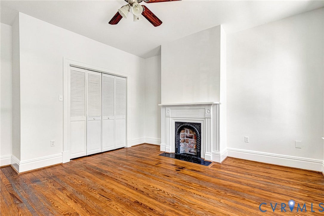 615 N 23rd Street, Church Hill Central, Richmond, VA 23223 Wood-finish flooring, white walls, louvered bi-fold closet doors, decorative fireplace with an ornate cast iron insert, and a ceiling fan with wood-finish blades