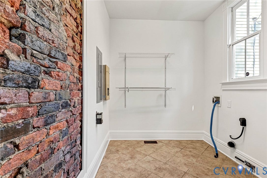 615 N 23rd Street, Church Hill Central, Richmond, VA 23223 Utility room featuring a brick accent wall, white painted walls, tan tile flooring, and adjustable wire shelving