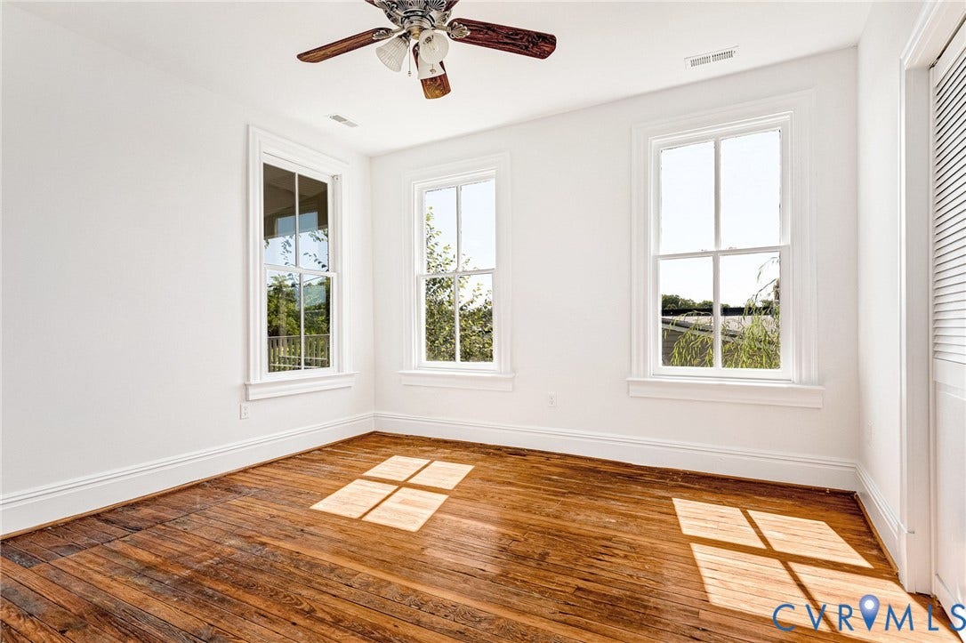 615 N 23rd Street, Church Hill Central, Richmond, VA 23223 Hardwood flooring, white painted walls, two large windows with white trim, and a ceiling fan with wood-finish blades